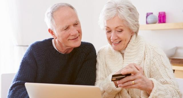 En man och kvinna som sitter framför en dator och ser glada ut, kvinnan har  en smarttelefon i handen