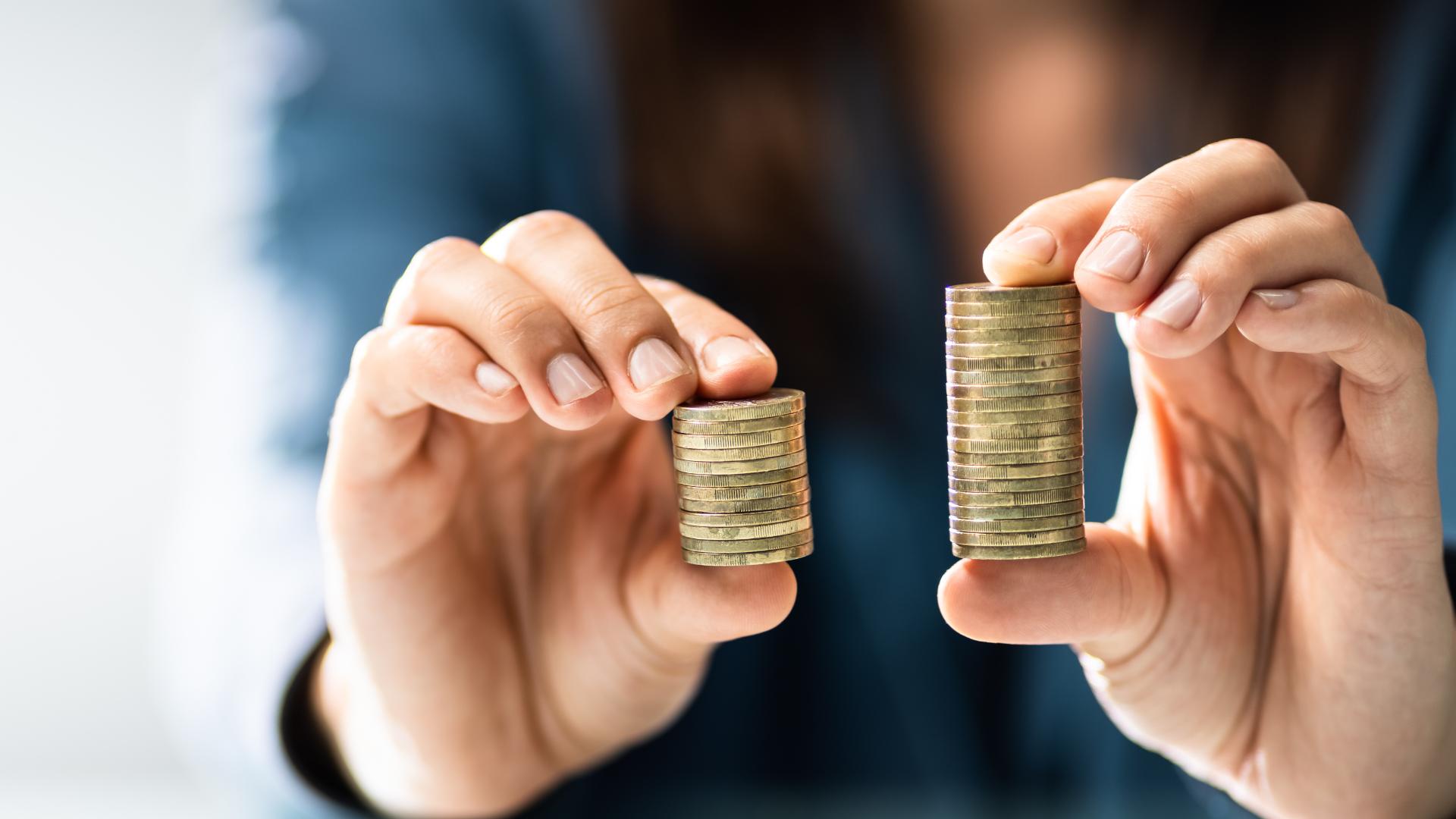En person håller två högar med mynt, en i varje hand. Högen i vänster hand är kortare än högen i höger hand. Bakgrunden är suddig.