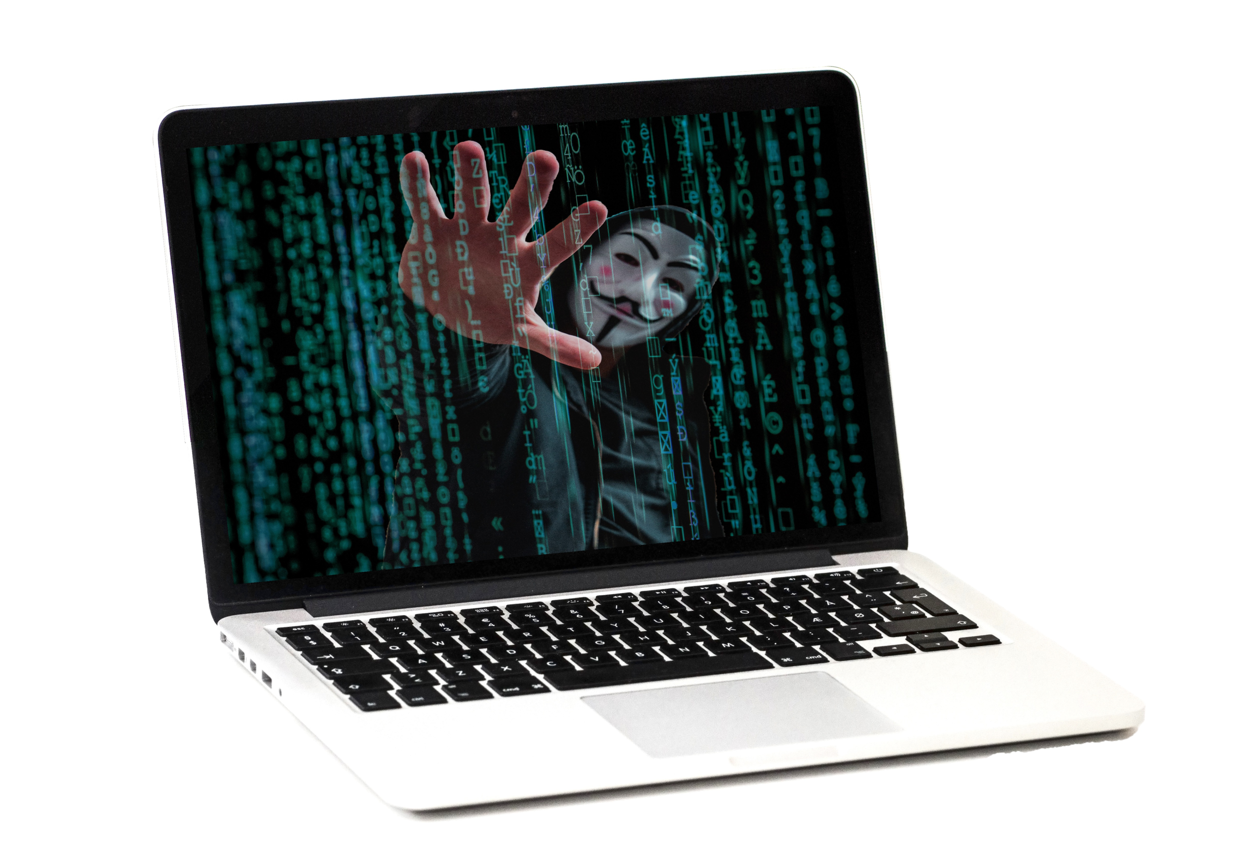 En laptopskärm visar en person i Guy Fawkes-mask med handen höjd mot en bakgrund av grön digital kod. Den bärbara datorn är placerad på en vit yta.
