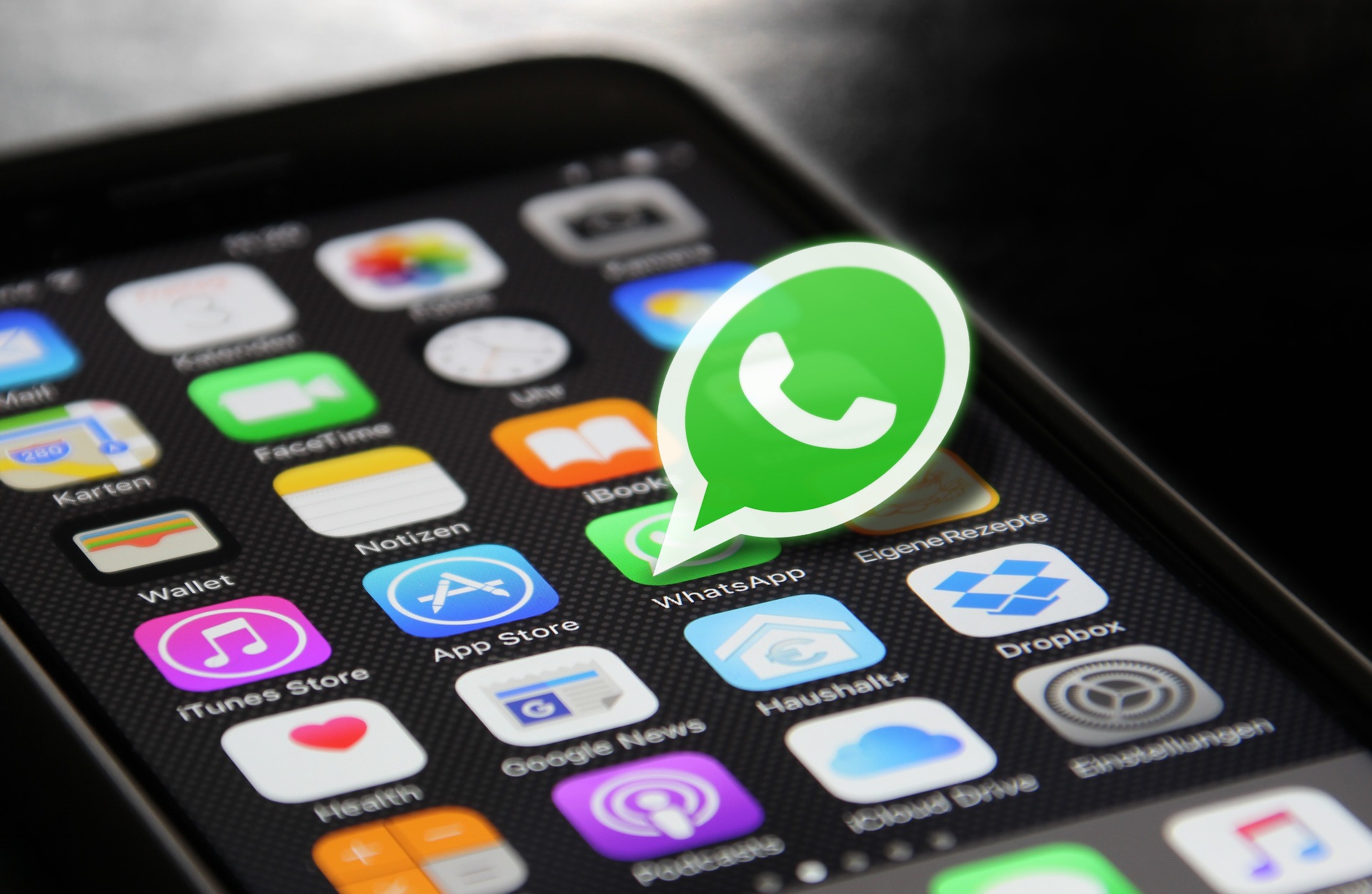 På en smarttelefonskärm visas olika appikoner, bland annat WhatsApp, App Store, iTunes Store och Google News, och en stor WhatsApp-logotyp är placerad ovanpå WhatsApp-ikonen.